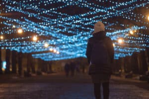 Woman walking down street with Christmas lights above