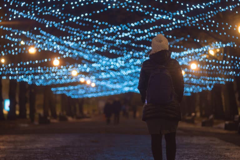 Woman walking down street with Christmas lights above