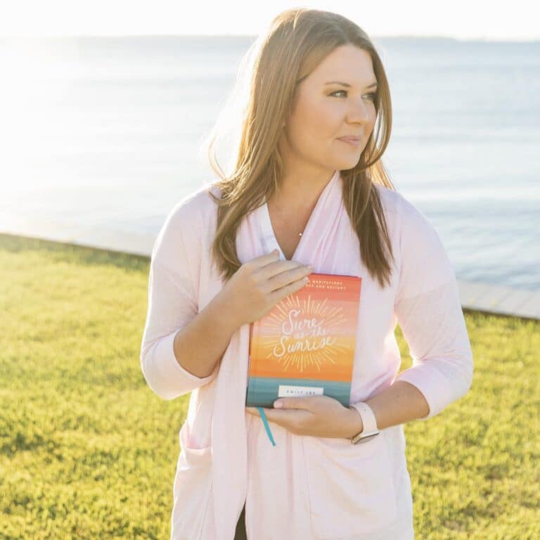 Emily Ley holding Sure as the Sunrise book by water's edge