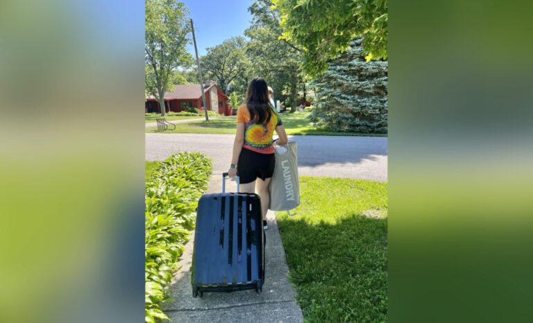 Teen walking down sidewalk with suitcase, color photo