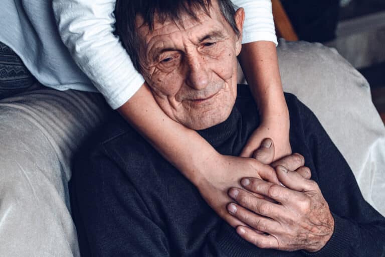 Elderly man and younger woman's arms around his neck