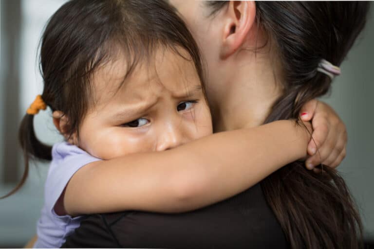 Sad child hugging mother's neck