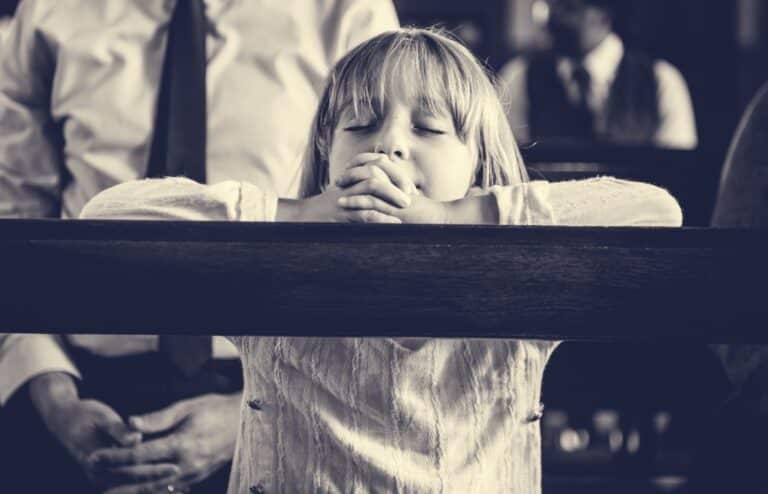 Child praying in church pew black and white photo