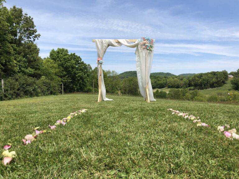 Square, wooden arch with floral and fabric in field, color photo