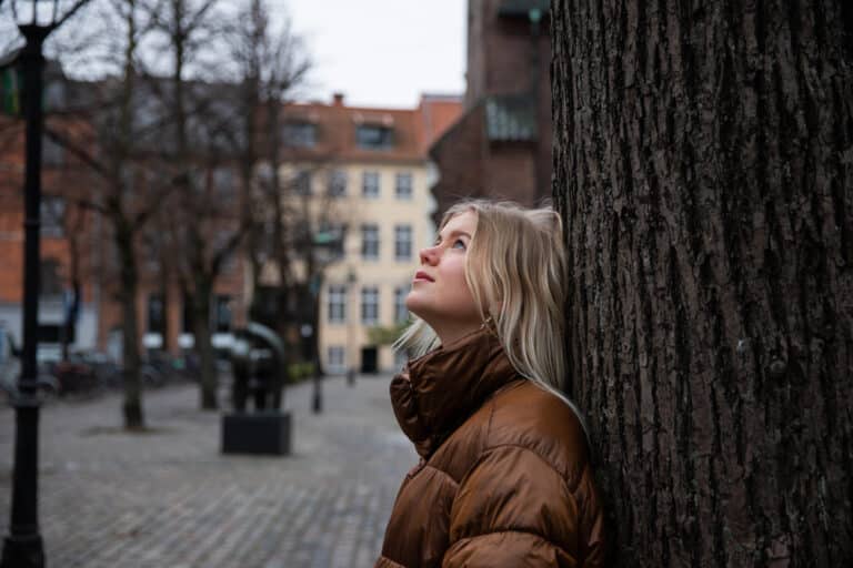 Woman looks up at sky outside in brown coat