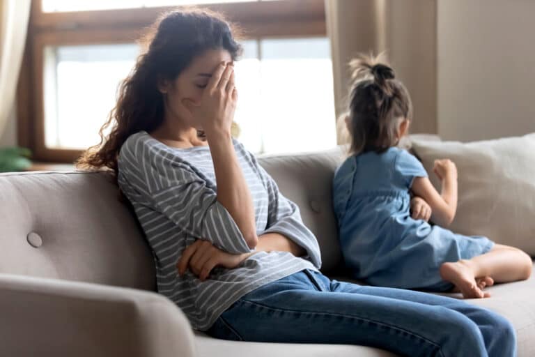 Woman tired on couch with child sitting next to her