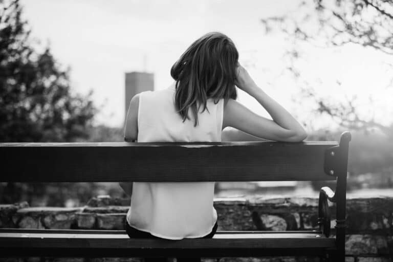 Woman sitting on park bench alone, black and white image