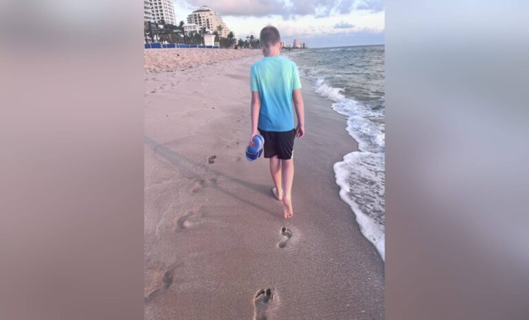 Teen boy walking along beach shore