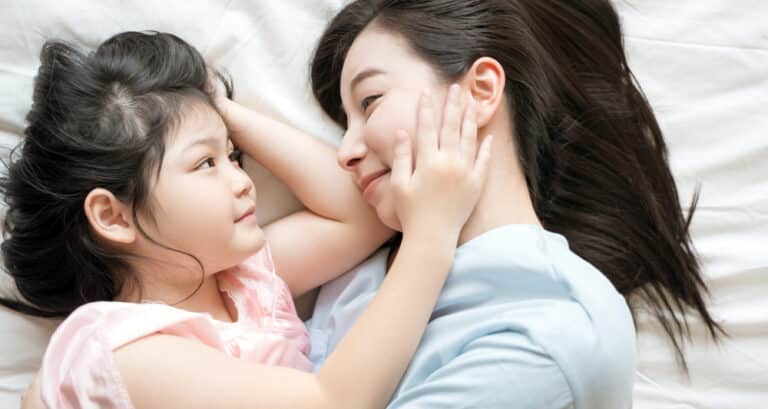 Child touching mother's face as they lie on a bed