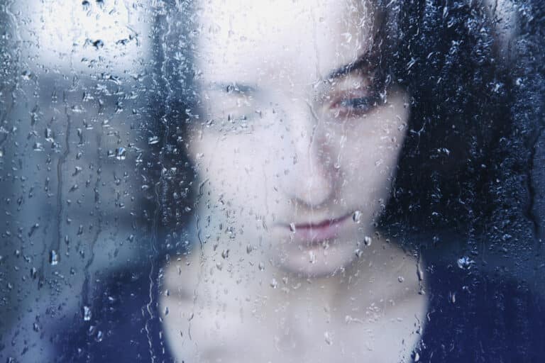 Sad woman through pane of rain covered glass