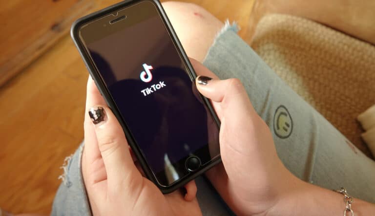 Teen hands holding smartphone with TikTok logo on screen