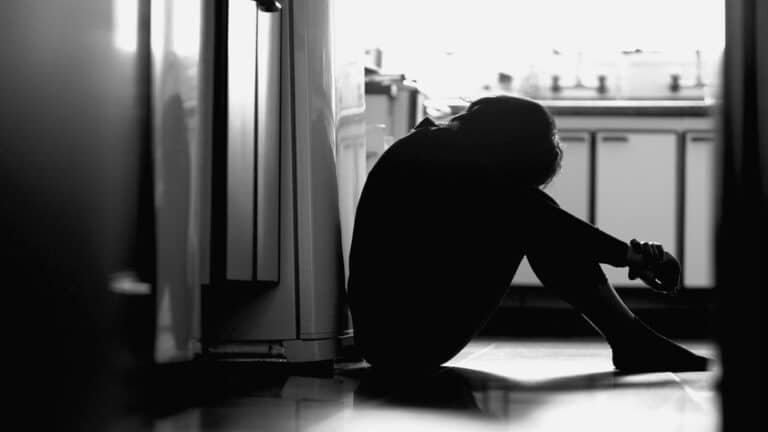 Depressed woman sitting on kitchen floor silhouette