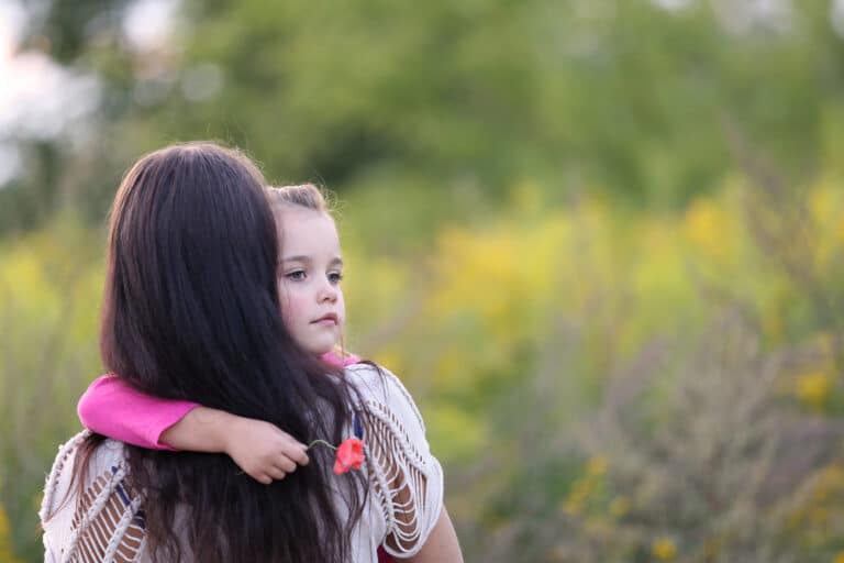 Woman holding young girl outside, blurred background