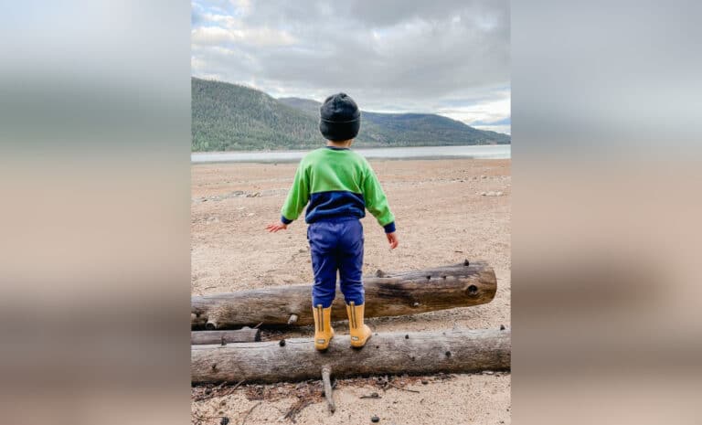 a little boy in rain boots standing on a log
