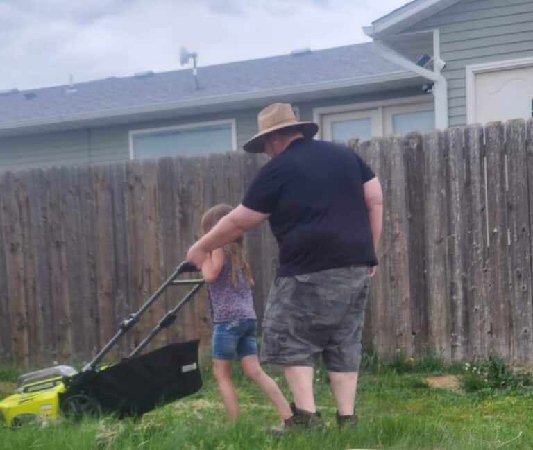 Dad helping daughter push lawnmower, color photo