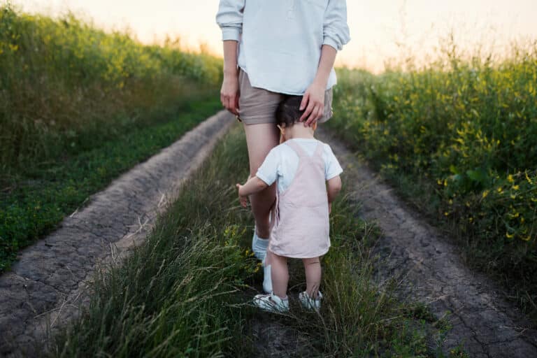 Toddler hugging mother's legs on path outside