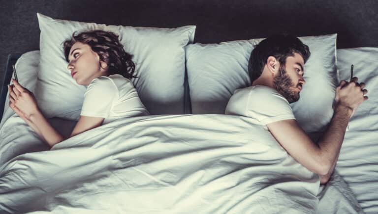 Couple with backs to each other in bed looking at phones