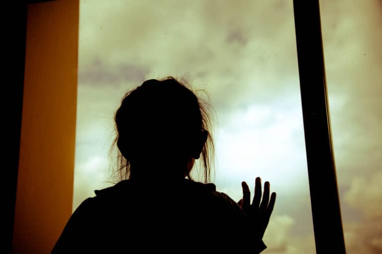 Silhouette of little girl with hand on window pane