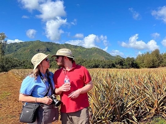 Mom and grown son look at each other outside, standing in a field wearing hats and hiking gear