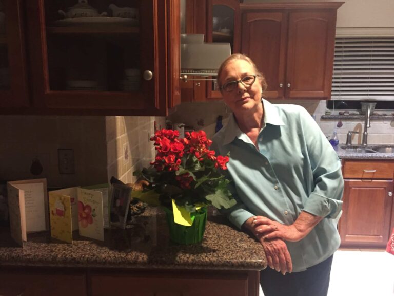 Woman standing in kitchen next to roses, color photo