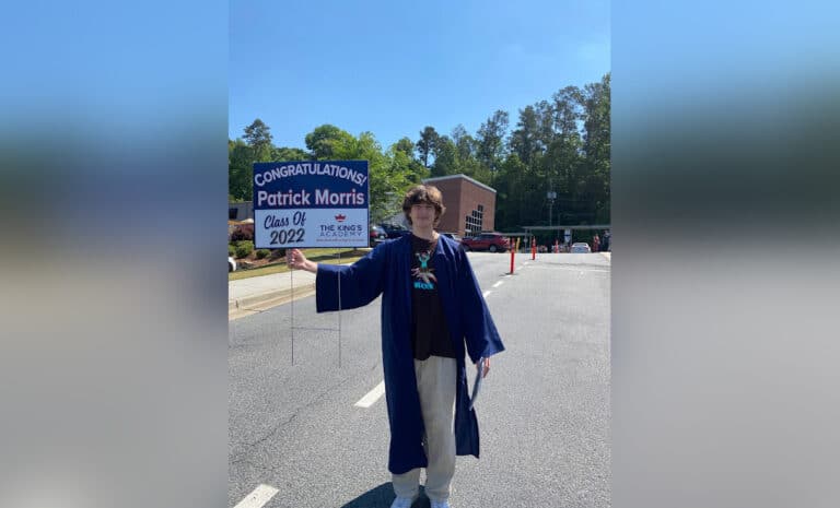 Teen boy in cap and gown, holding graduation sign, color photo