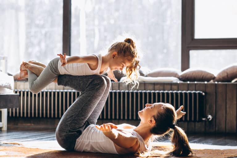 Woman exercising with child, lifting little girl on her legs doing yoga