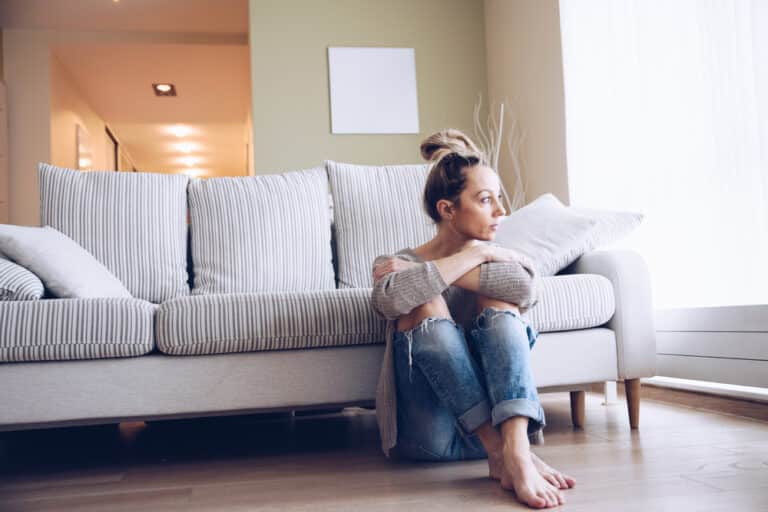 Woman sitting on floor by couch looking sad