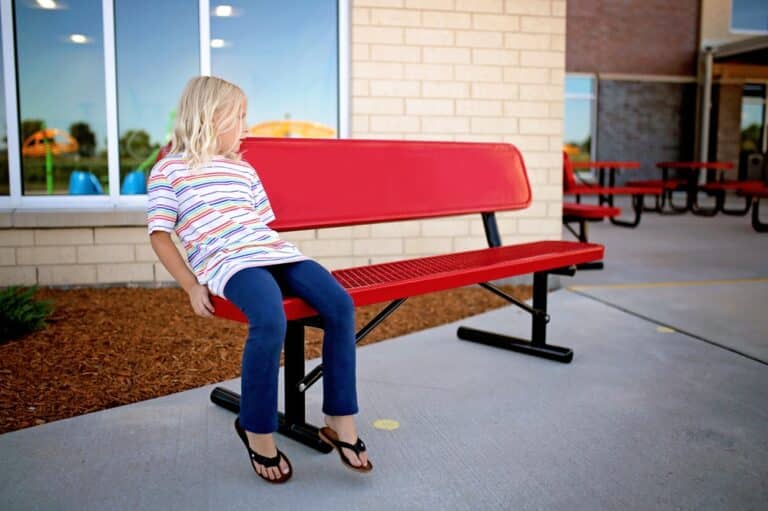 Little girl sitting on red bench alone at school