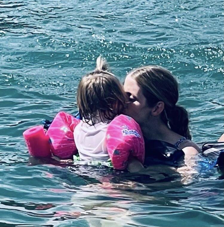 mom holding her daughter wearing a puddle jumper in the lake