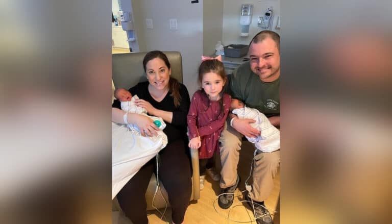 Mother and father holding twin newborns with toddler girl in between them, smiling in hospital room