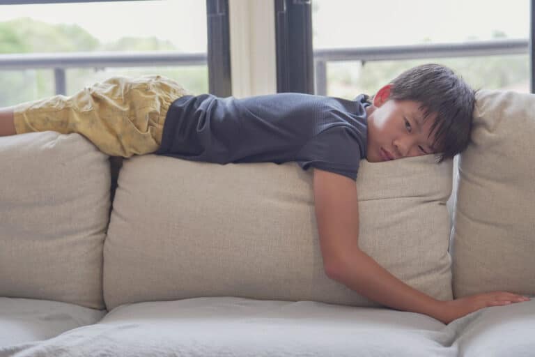 Tween boy lying on back of couch cushions in front of a window