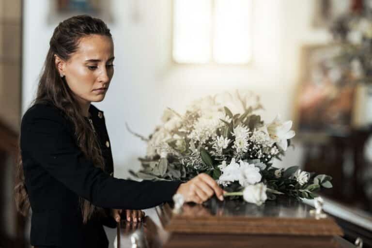 Sad woman placing a white flower on a closed casket
