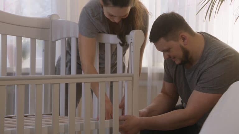Parents assembling white wooden baby crib and smiling