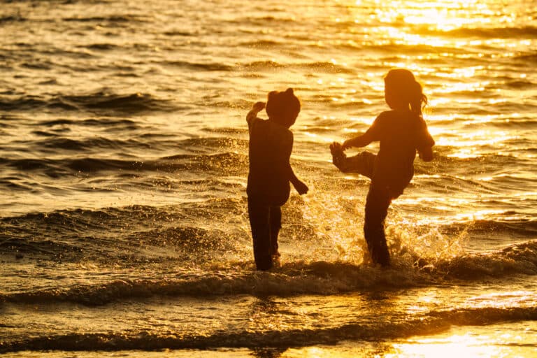 Silhouette of young girls playing in water at sunset