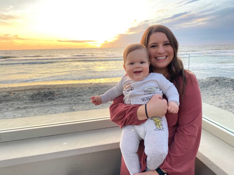 Mother holding baby with ocean and sunset in the background, color photo
