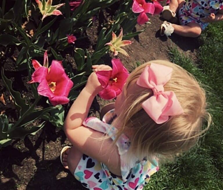 Toddler smelling flowers in garden, color photo