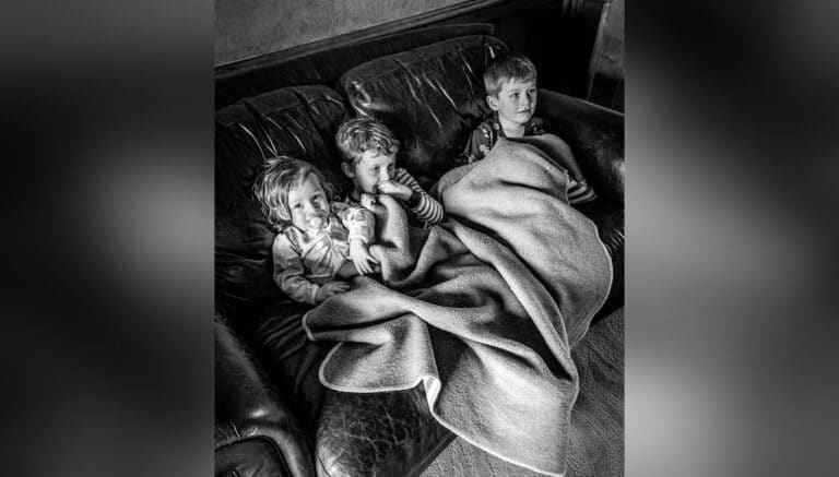 Three children cuddled under blankets on a couch, black-and-white photo