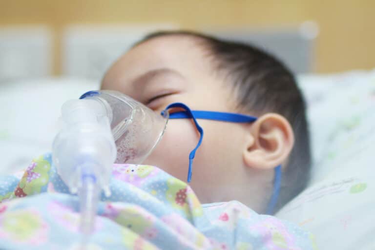 Toddler boy wearing nebulizer mask in hospital bed
