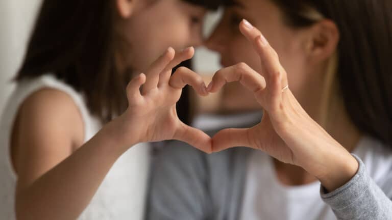 Mother and daughter make heart with fingers