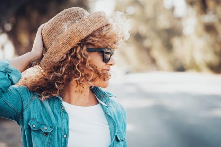 Side view of woman wearing hat and sunglasses outside smiling