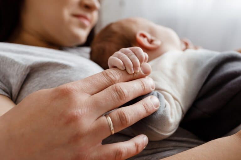 Mother holding hand of newborn lying on her chest