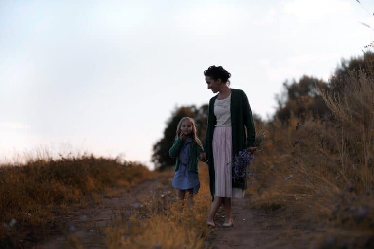 Young mother walking with daughter outside on path at dusk