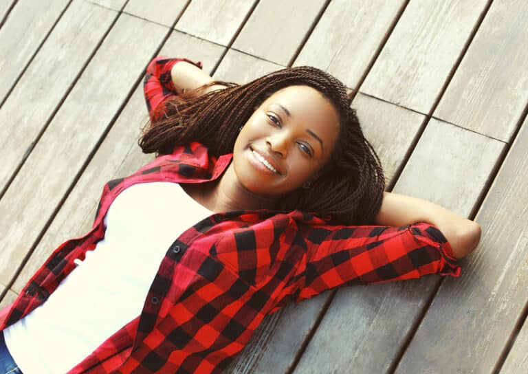 Young girl smiling with arms crossed behind her head, lying on wood decking