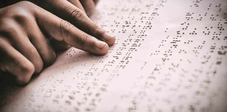Fingers of a child reading braille in a book