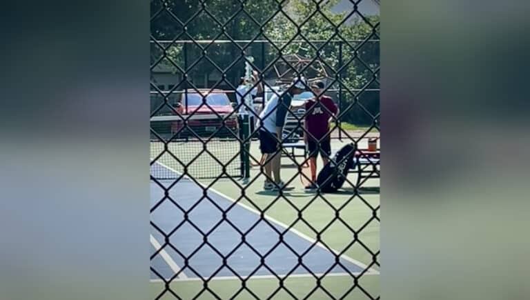 Coach talks to young tennis player on sidelines of court