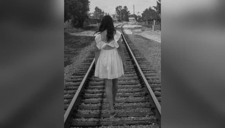 Black and white photo of teen girl walking down railroad track