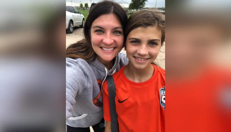 Mom and young daughter in soccer gear smiling at camera