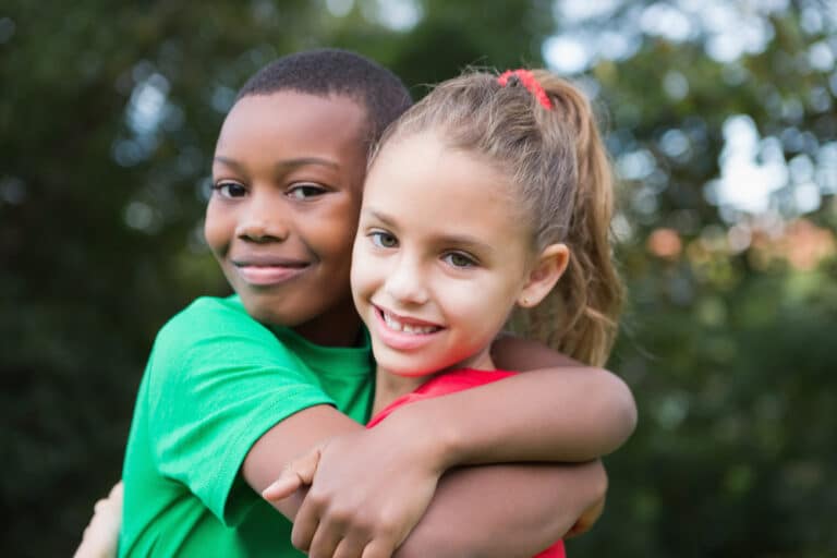 Two school age kids smiling with arms around each other