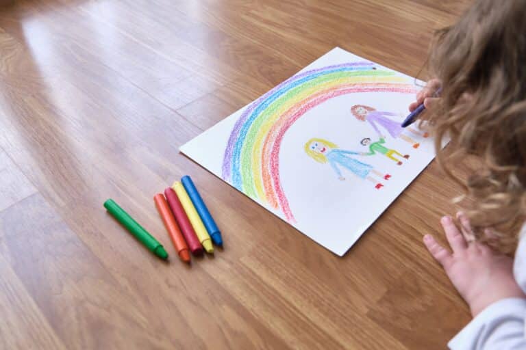 Child drawing rainbow and family holding hands of child