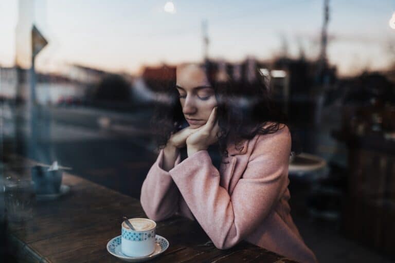 Sad woman sitting by coffee shop window alone looking down
